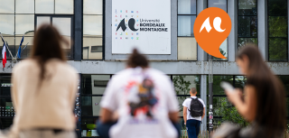 3 &eacute;tudiantes assises de dos sur un banc et un &eacute;tudiant qui marche vers un b&acirc;timent de l'Universit&eacute; Bordeaux Montaigne
